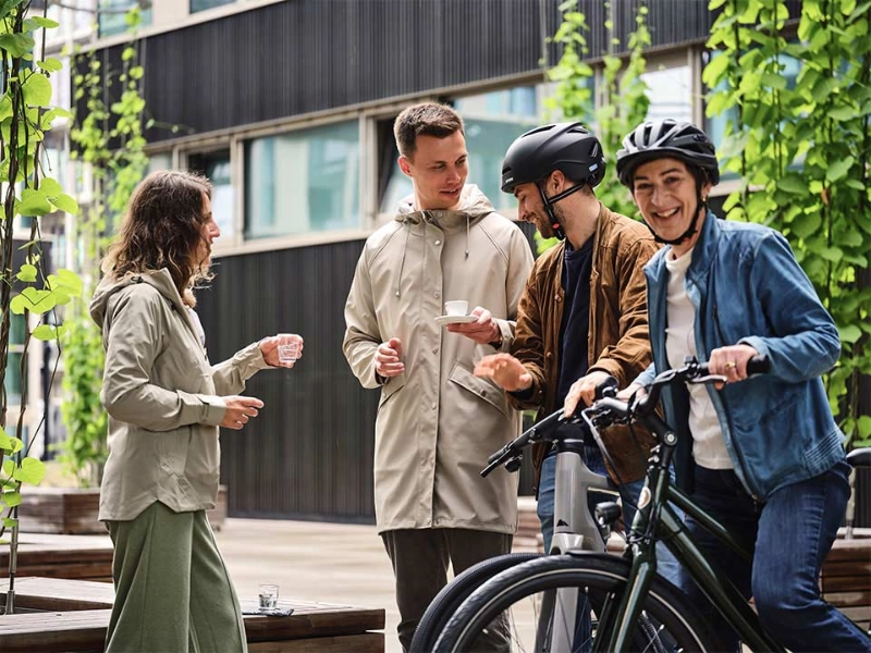 Ein JobRad Team aus vier Personen trinkt Kaffee auf dem JobRad-Campus, eine Frau aus dem Team sitzt auf dem Fahrrad Ein JobRad Team aus vier Personen trinkt Kaffee auf dem JobRad-Campus, eine Frau aus dem Team sitzt auf dem Fahrrad